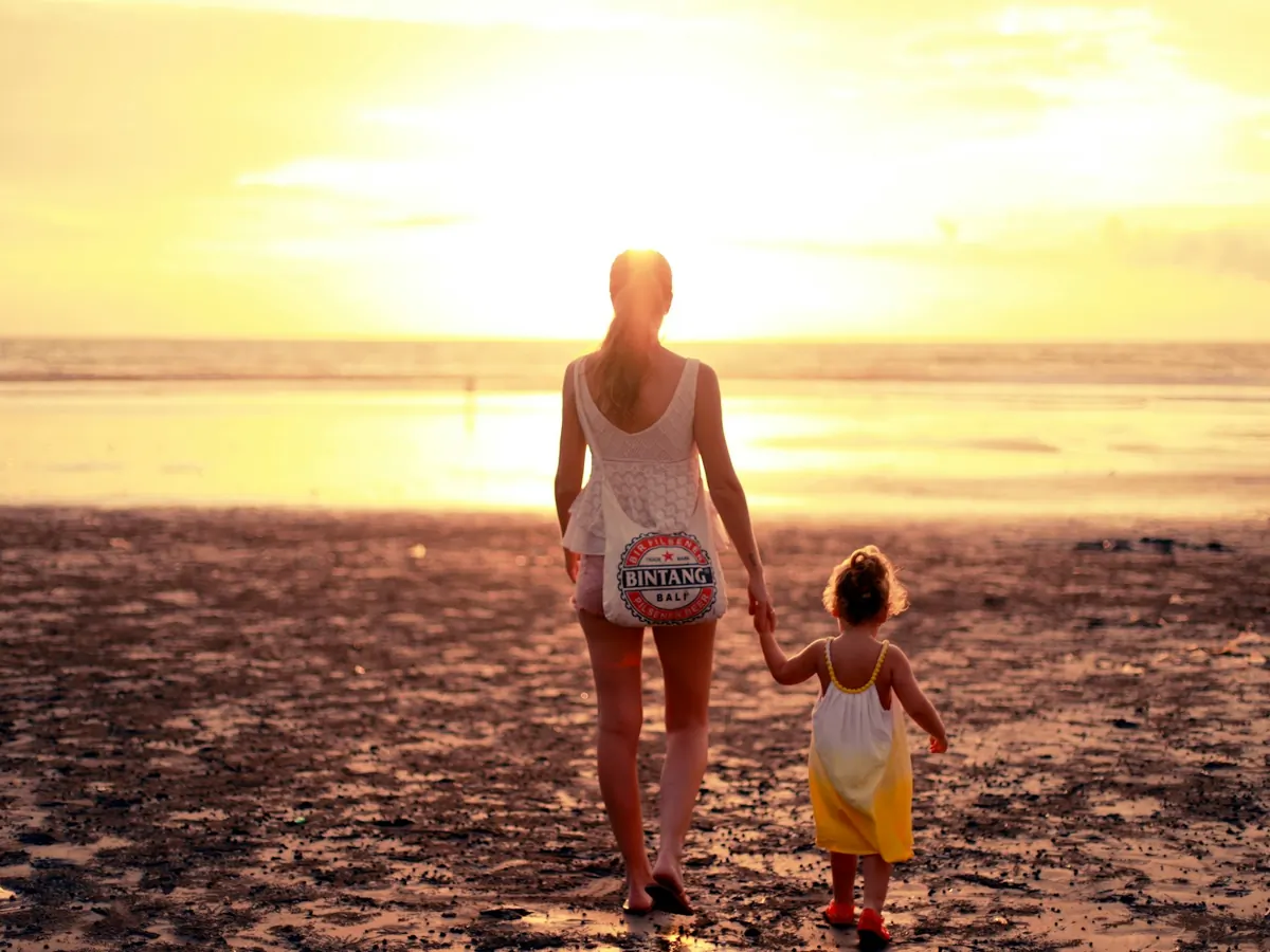 Mother and child walking on the beach at sunset